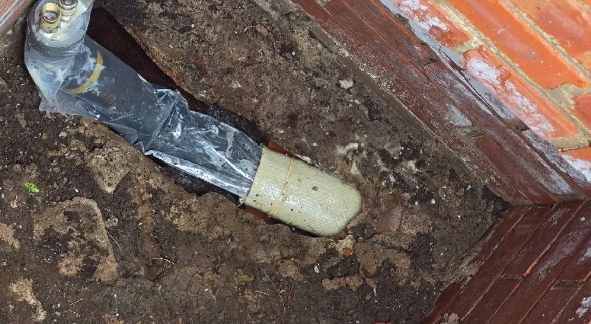 A resin-soaked patch liner on its packer, at the mouth of a pipe inside an opened brick chamber.